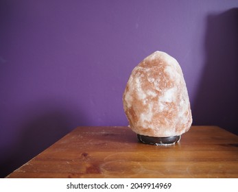 Himalayan salt rock lamp on a desk, purple wall behind. Close up lamp. 