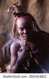 Himba woman taking daily smoke bath inside her hut in a traditional Himba village near Kamanjab, northern Namibia, Africa.