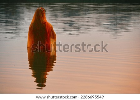 Hindu devotee offering prayers to sun god standing in water according to hindu rituals during Chhath Puja Festival. Chath Puja rituals                             