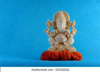 Hindu God Ganesha. Ganesha Idol On Blue Background With Flowers. 