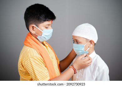 Hindu Kid Helping His Muslim Friend To Properly Wear Medical Face Mask On Gray Background To Protect From Coronavirus Or Covid-19 Pandemic - Concept Of Religious Harmony And Unity