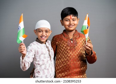Hindu Muslim Children holding Indian flag on gray background - concept of kids celebrating Indian Republic or Independence day, Religious unity and patriotism.
