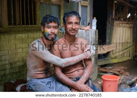 Hindu young devotee painted his body and faces with mud and colours in Durgapuja festival , south asian young boy hugging his father, a happy family photo 