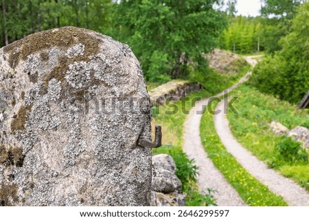 Hinge on a boulder as a gatepost by an old dirt road with stone walls in the countryside