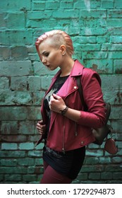 Hip Portrait Of A Beautiful Girl With Short Pink Hair In A Pink Jacket On A Background Of A Turquoise Wall. Punk / Freak Style. Daylight Shooting, Shallow Depth Of Field