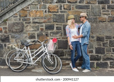 Hip Young Couple Hugging By Brick Wall With Their Bikes On A Sunny Day In The City