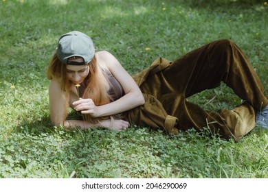 Hip-hop Girl In Brown Corduroy Pants Sniffing Yellow Flower Lying On Green Grass