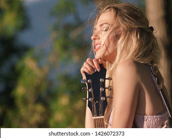 Hippie looking young adult woman wearing gypsy outfit having acoustic guitar. Female playing music in park.
