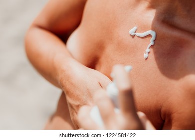 Hippie young ginger woman sunbathing topless on a beach, using suntan cream