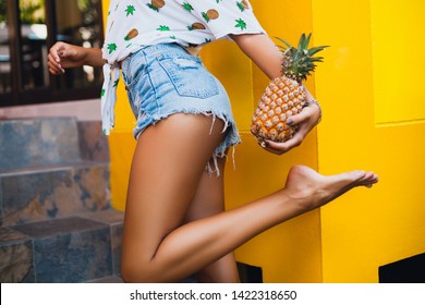 hips in jeans shorts of attractive woman on summer vacation, skinny figure sexy body, holding pineapple, fruit diet detox, tanned skin, yellow background