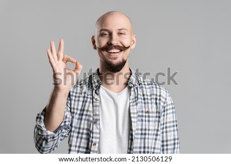 hipster bald man with beard and mustache wears checkered shirt, showing ok isolated on gray background. Sincere emotions concept