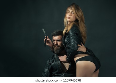 Hipster with beard and sexy girl holds straight razor. Couple of sexy girl and brutal bearded hipster with mustache, black background. Barber with straight razor works on haircut. Barber concept.
