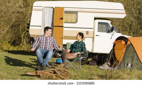 Hipster boyfriend kissing his girlfriend hand while sitting on camping seats in front of their vintage camper van. Relaxing Week-end - Shutterstock ID 1553585885