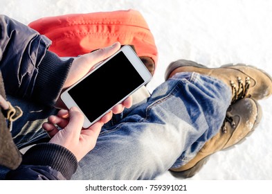 Hipster business man sitting in snow using white mobile smart phone, oled display, on wild nature, winter vacation, hiking, traveling, backpacker, warm clothes in Christmas time on a cold winter day - Shutterstock ID 759391021
