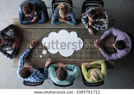 Hipster business teamwork brainstorming planning meeting concept, man tells his opinion, people sitting around the table with white paper shaped like dialog cloud