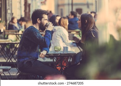Hipster couple drinking coffee in Stockholm old town. They're sitting face to face. The man is wearing a blue sweater and the woman a striped shirt with black leather jacket. See-through shot. - Shutterstock ID 274687205