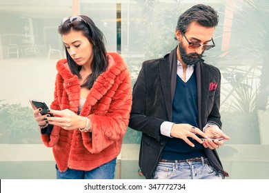 Hipster couple in sad moment ignoring each other using mobile phones - Concept of apathy sadness addicted to new technologies - Boyfriend and girlfriend break up with smartphones addiction