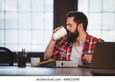 Hipster drinking coffee at desk in creative office - Powered by Shutterstock