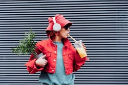 Hipster Fashion Woman In Bright Clothes, Heart Shaped Glasses, Headphones, Bucket Hat Drinking Fruity Flavored Tapioca Bubble Tea And Holding Green Potted Plant On The Gray Striped Wall Background.