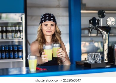 Hipster girl bartender serving fresh lemonade behind counter at outdoor bar during summer festival - Shutterstock ID 2182063547