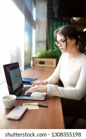 Hipster Girl Experienced Business Planning Expert Working On Laptop Computer While Sitting In Modern Office Interior. Female With Cool Look Creative Web Content Writer Checking E-mail On Notebook 