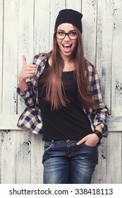 Hipster Girl In Glasses And Black Beanie With Thumbs Up On The Wooden Background