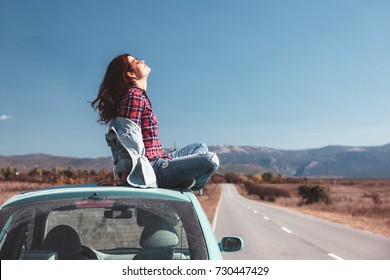 Hipster girl relaxing on the car roof in her autumn road trip, carefree and enjoying freedom and travel. Wanderlust concept scene.