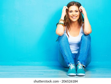 Hipster girl sitting on floor against blue background.