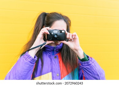 Hipster girl takes pictures with a film camera. Portrait of a young girl in a bright jacket near the yellow wall. Analog Shooting Camera, Fashion Styl. - Shutterstock ID 2072960243
