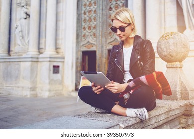 Hipster Girl With Trendy Look Is Reading Electronic Book On Portable Touch Pad, While Is Sitting Outside The Museum. Beautiful Woman Is Watching Movie On Digital Tablet, While Relaxing After Strolling