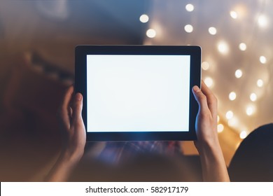 Hipster girl using tablet technology in home atmosphere, person holding computer on background glow illumination, female hands text on relax glitter xmas decoration, mock up templates, blur