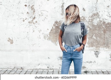 Hipster Girl Wearing Blank Gray T-shirt, Jeans And Backpack Posing Against Rough Street Wall, Minimalist Urban Clothing Style, Mockup For Tshirt Print Store