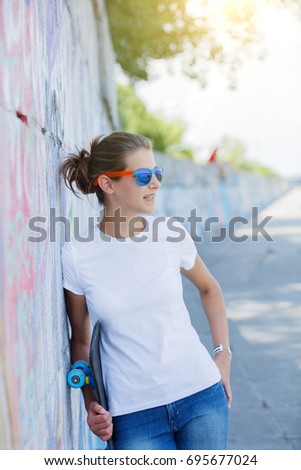 Hipster girl wearing blank white t-shirt, jeans and sunglasses posing against rough street wall, minimalist urban clothing style, mockup for tshirt print store