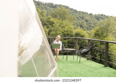 Hipster girl working with a laptop at home office in a glamping in the mountains with great views. - Powered by Shutterstock