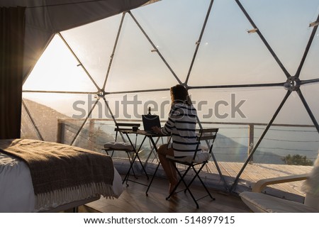 Hipster girl working with a laptop at home office in a glamping in the mountains with great views