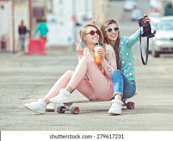 Hipster girlfriends taking a self photo on the street seating on skateboard  in fashion clothes eternalizing the moment with modern digital camera