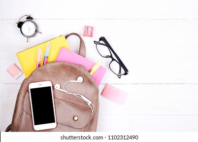 Hipster Grey Leather Backpack, Full Of School Supplies, Blank Screen Cell Phone, Earphones, Pink & Yellow Notebook, Glasses, Mini Alarm Clock. Back To School Concept. Close Up, Copy Space, Flat Lay.