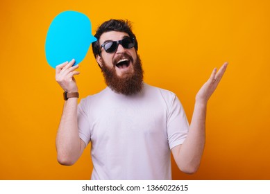 A hipster guy in sunglasses holding a bubble speech over yellow background  - Shutterstock ID 1366022615
