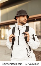 Hipster Handsome Man Model With Bucket Hat In White Sporty Jacket With Backpack Walks On The Street And Travel