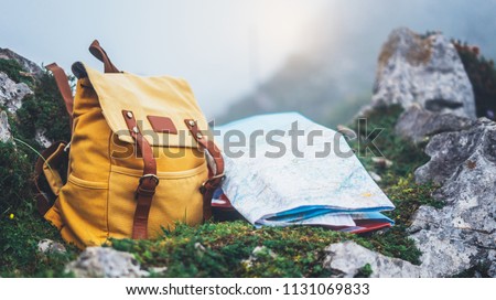 Hipster hiker tourist yellow backpack and map europe on background green grass nature in mountain, blurred panoramic landscape, traveler relax holiday concept, view planning wayroad in trip vacation 