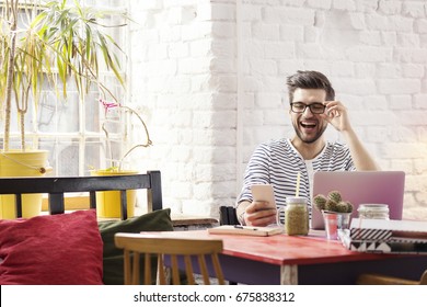 Hipster laughing while browsing social media on the phone in raw interior