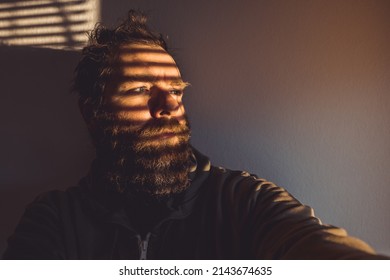 Hipster Looking Man Hiding Behind The Venetian Blinds Or Window Shades. Cool Guy Wearng A Hoodie In An Interesting Lighting.