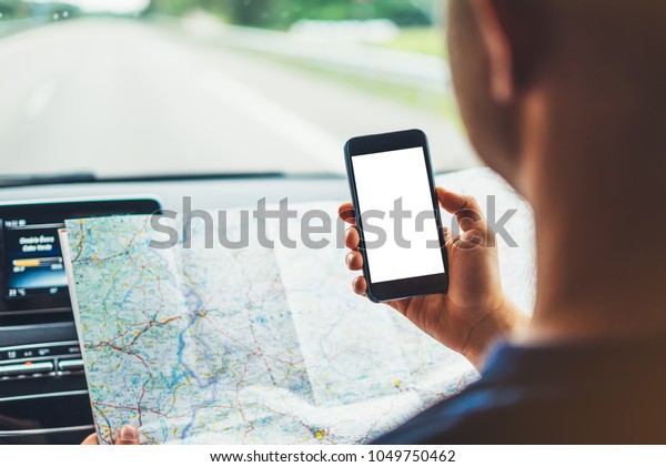 Hipster looking on navigation map in car, tourist\
traveler driving and holding in male hands smartphone gps with\
clean screen display, panoramic view way road, trip in\
transportation from window\
auto