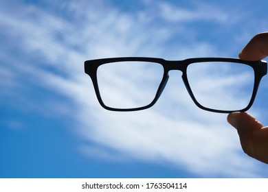 Hipster Male Hand Hold Glasses Without Glass Above Blue Cloudy Sky Background.