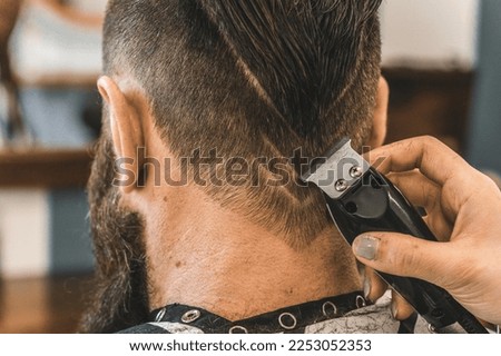 Hipster man at barbershop salon getting beard and hair cut - Hairdresser woman using hair clipper to modern cut with geometric drawing on the nape - Barber shop concept
