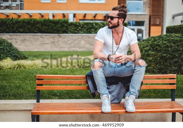 Hipster with man bun sitting on the park bench on a\
sunny day