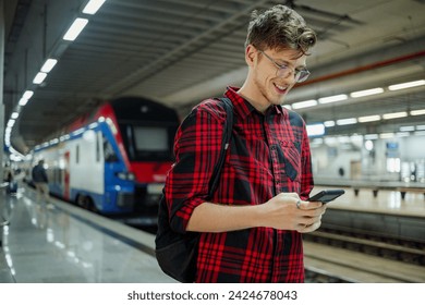 Hipster man commuting to work or a school by a train or a subway while using a phone. Young male is reading emails or typing a message on a mobile phone while at the station. Copy space. - Powered by Shutterstock