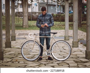 Hipster Man With A Fixie Bike And Smartphone In A Park Outdoors