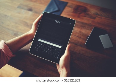 Hipster man hands holding digital tablet with empty blank screen for your text message, business person browsing internet or connecting to wireless via touchscreen pad sitting at brown wooden table