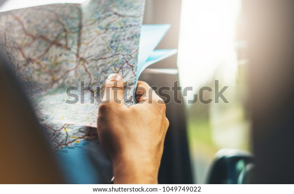 Hipster man holding in male hands and looking on\
navigation map in auto, tourist traveler hiker driving on\
background panoramic view way road, trip in transportation, person\
on backdrop window auto